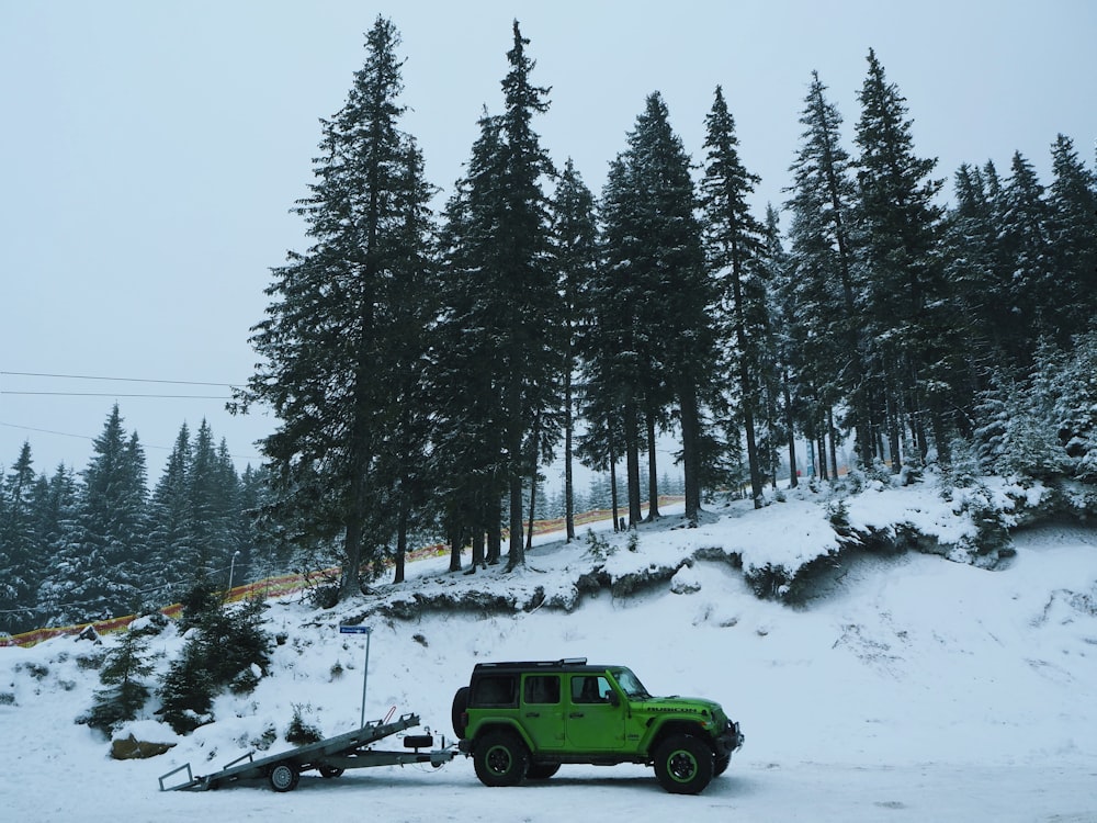 green truck on snow covered ground near trees during daytime
