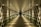 A long, symmetrical corridor with reflective glass walls and a patterned ceiling, illuminated by warm artificial lights. The perspective converges towards a distant dark opening, creating a sense of depth and infinity.