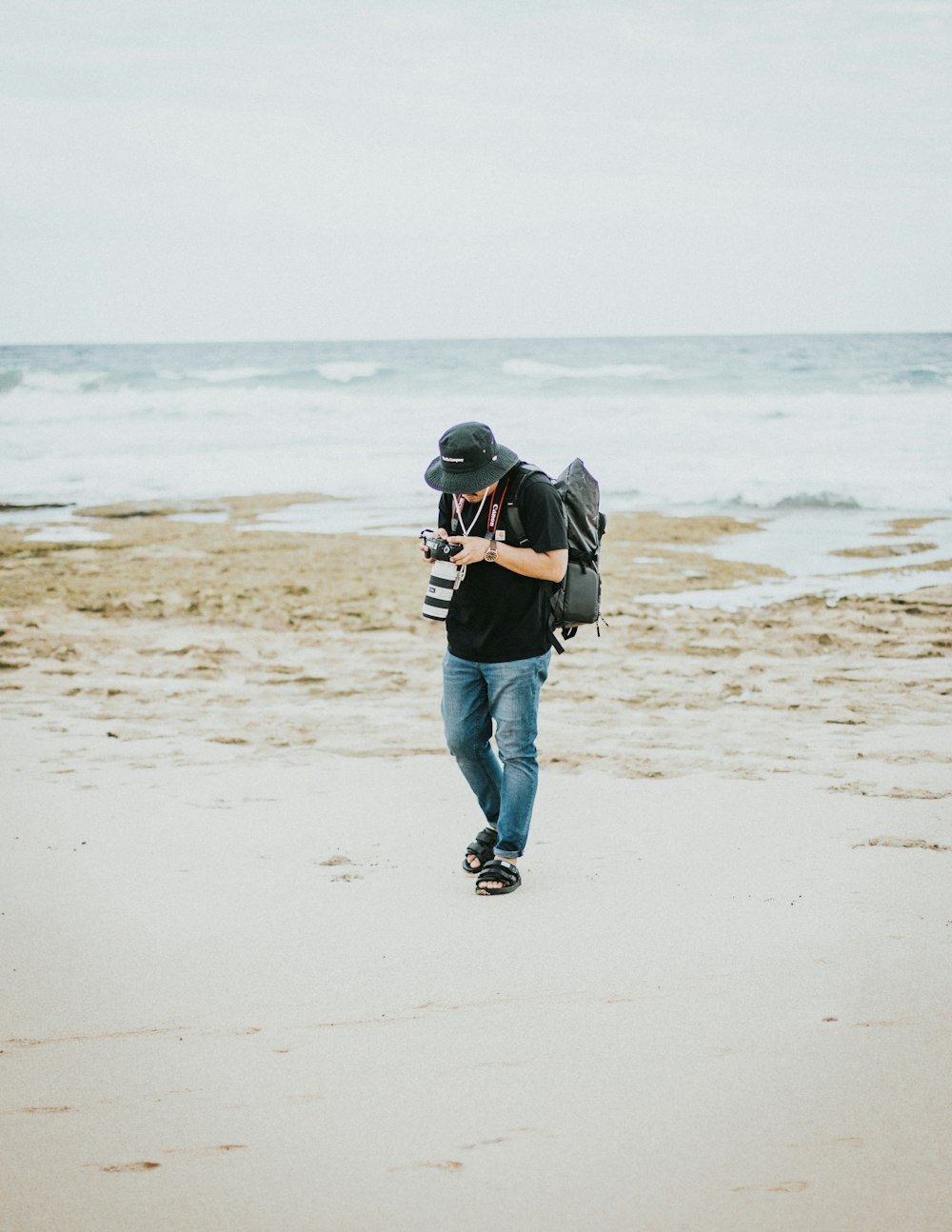 man in black jacket and blue denim jeans walking on beach during daytime