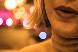 An artistic close-up of a person's mouth and chin, with soft lighting and a bokeh effect in the background featuring circular light blurs.