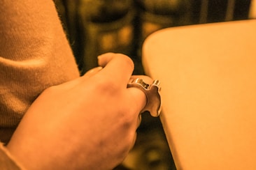 A close-up of a hand holding a metallic keychain shaped like an apple. The lighting gives a warm, yellowish tint to the entire scene.