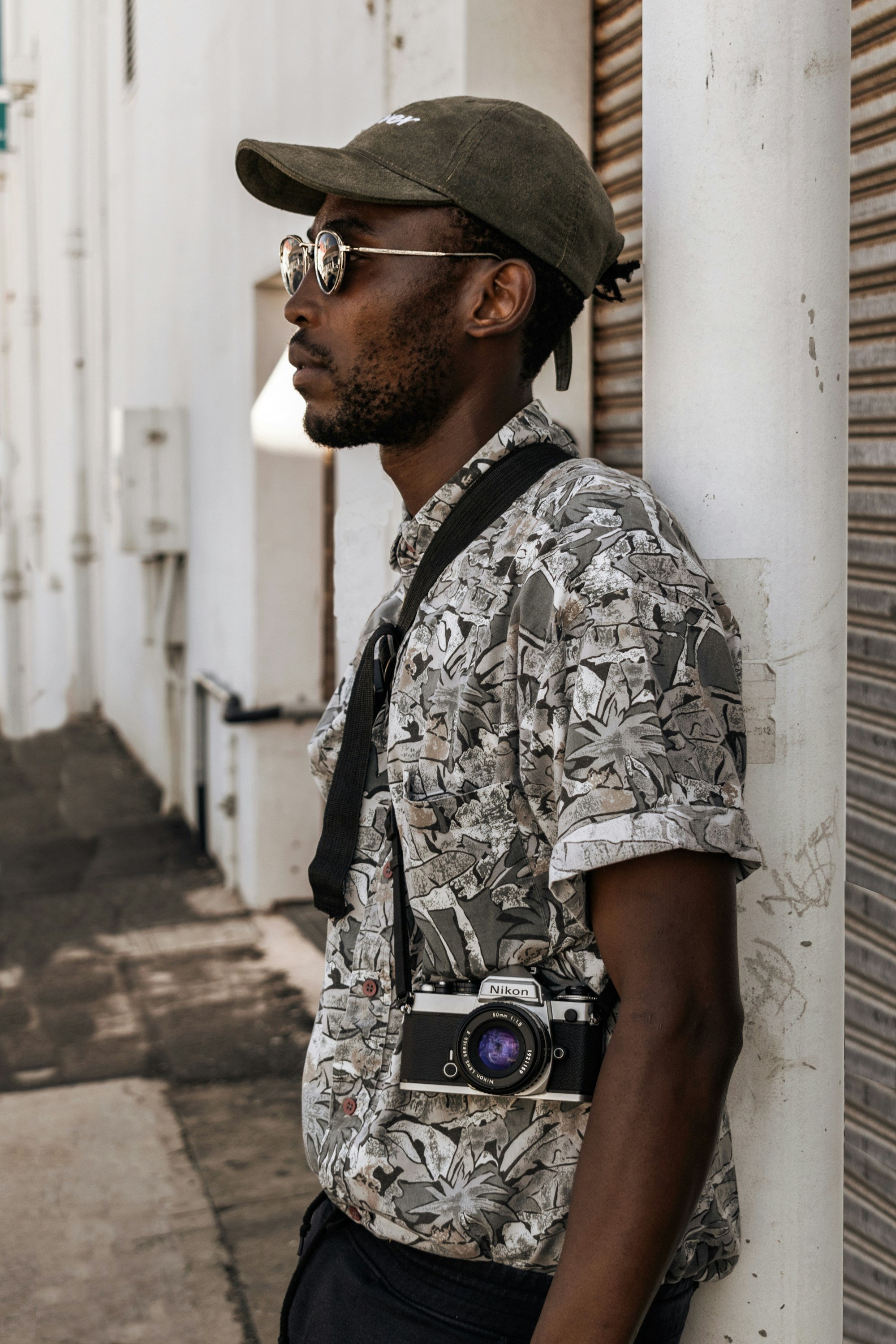 Man in black and white floral shirt and black hat standing beside white