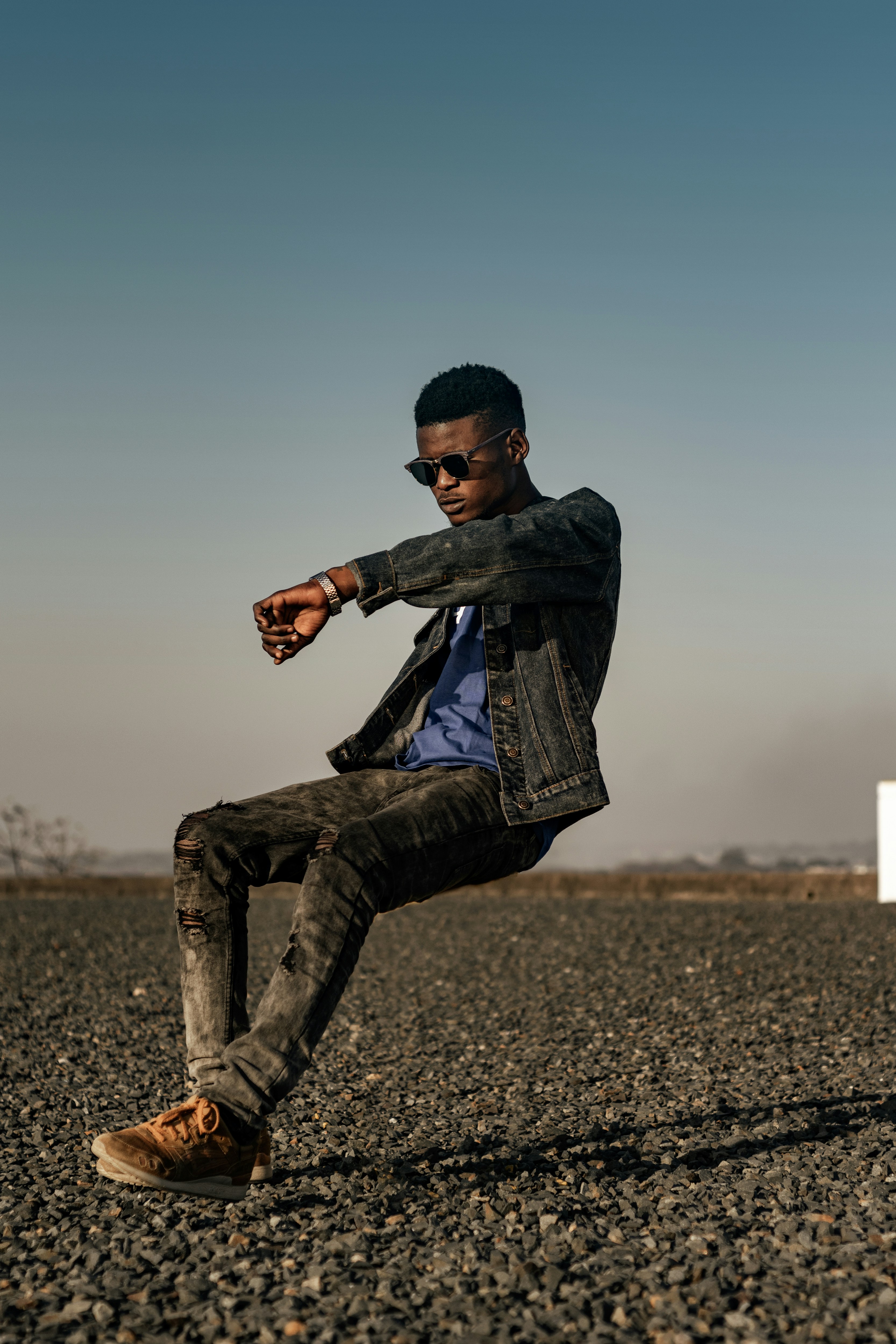 man in black and gray plaid dress shirt and black denim jeans sitting on gray concrete