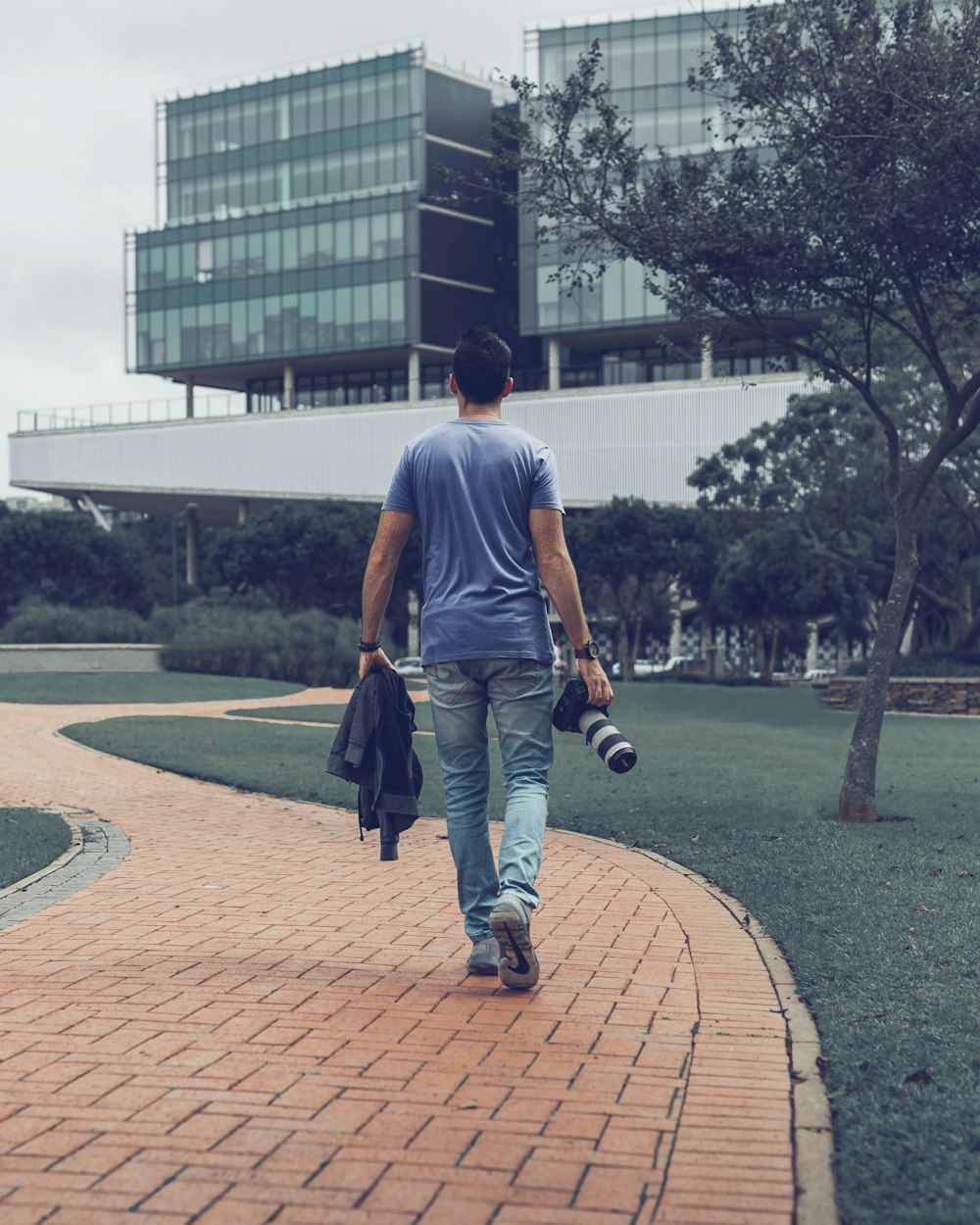 man in blue t-shirt and blue denim jeans walking on brown brick pathway during daytime