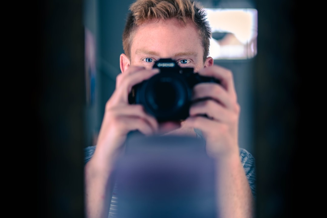 man in blue crew neck t-shirt holding black dslr camera