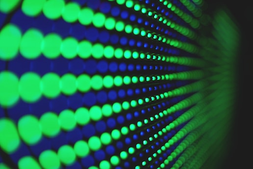 A close-up pattern of glowing green and blue circular lights arranged in a geometric grid. The circles vary in size and are evenly distributed across a dark background, creating a vibrant and hypnotic visual effect.
