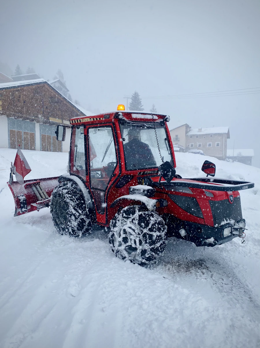 Rød traktor med brøyteskjær i tett snøvær