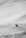 A snowboarder is captured mid-air performing a trick on a steep snow-covered slope. The landscape is vast and predominantly composed of untouched snow, creating a sense of openness and adventure.