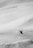 A snowboarder is captured mid-air performing a trick on a steep snow-covered slope. The landscape is vast and predominantly composed of untouched snow, creating a sense of openness and adventure.