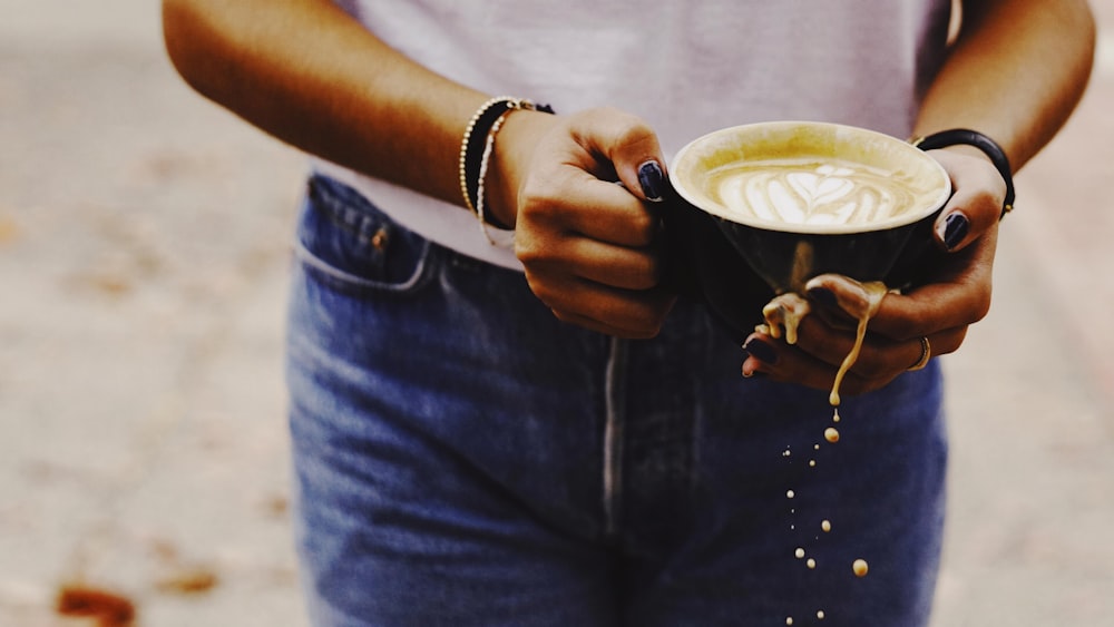 person in blue denim jacket holding white ceramic mug with coffee