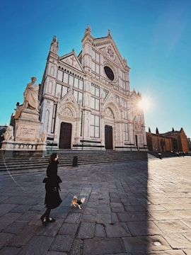 woman in black jacket walking on sidewalk near cathedral during daytime