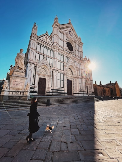 woman in black jacket walking on sidewalk near cathedral during daytime