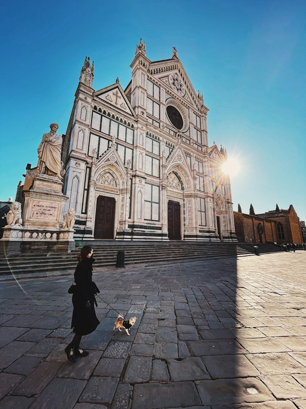 woman in black jacket walking on sidewalk near cathedral during daytime