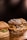 Three gourmet hamburgers placed on a wooden surface, featuring a variety of toppings such as melted cheese, onions, and bacon. The buns have a rustic appearance with visible flour dusting.