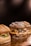 Three gourmet hamburgers placed on a wooden surface, featuring a variety of toppings such as melted cheese, onions, and bacon. The buns have a rustic appearance with visible flour dusting.