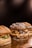Three gourmet hamburgers placed on a wooden surface, featuring a variety of toppings such as melted cheese, onions, and bacon. The buns have a rustic appearance with visible flour dusting.