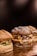 Three gourmet hamburgers placed on a wooden surface, featuring a variety of toppings such as melted cheese, onions, and bacon. The buns have a rustic appearance with visible flour dusting.