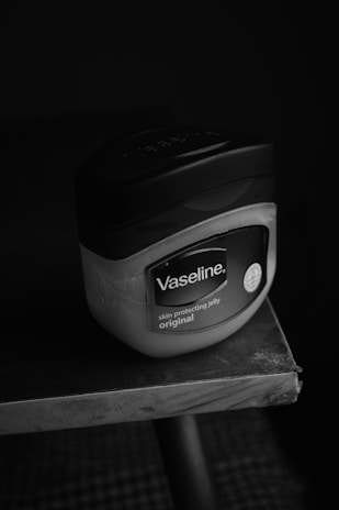 A container of Vaseline skin protecting jelly, labeled as original, is placed on the edge of a table. The background is dark, drawing attention to the product's packaging.