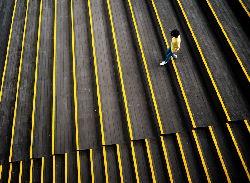 man in white shirt and blue denim jeans walking on gray and yellow striped tunnel