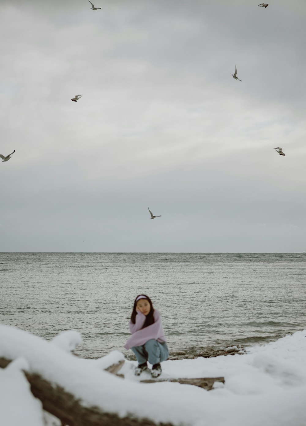 girl in pink tank top sitting on beach shore with birds flying over the sea during