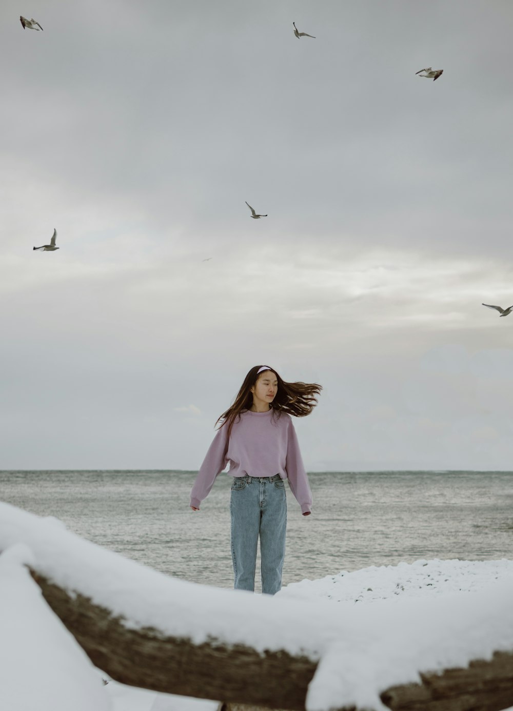 woman in pink long sleeve shirt and blue denim jeans standing on white sand during daytime