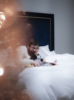 man in black suit lying on bed beside woman in white long sleeve shirt