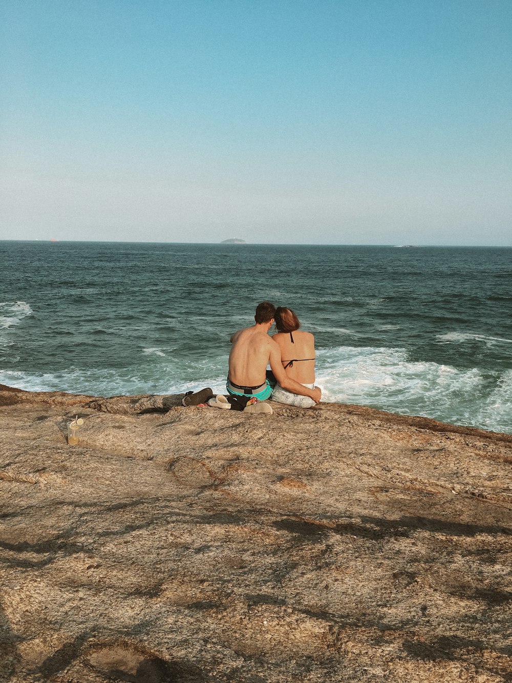 femme en bikini noir assis sur un rocher brun près de la mer pendant la journée