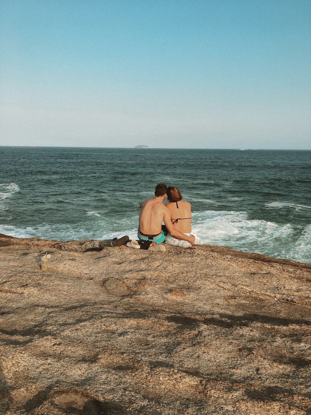 woman in black bikini sitting on brown rock near sea during daytime