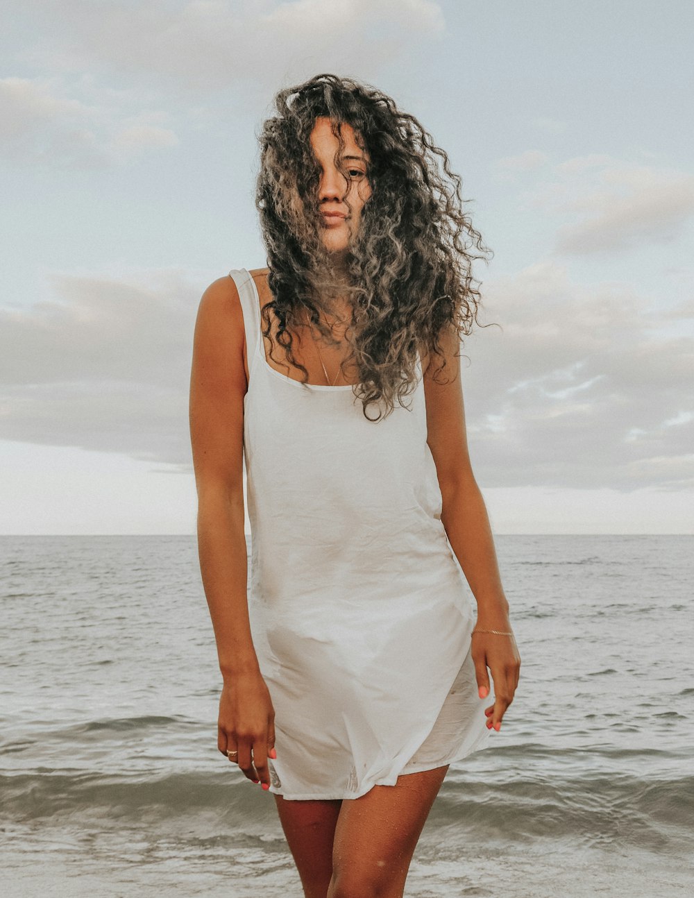 woman in white tank top standing on sea shore during daytime