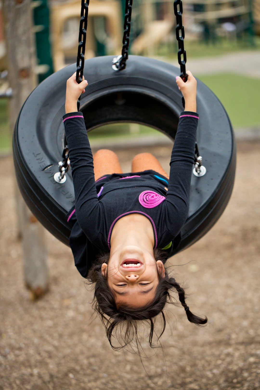 girl in black and pink long sleeve shirt riding on black and gray swing during daytime