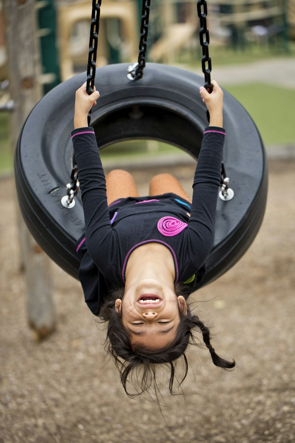 girl in black and pink long sleeve shirt riding on black and gray swing during daytime