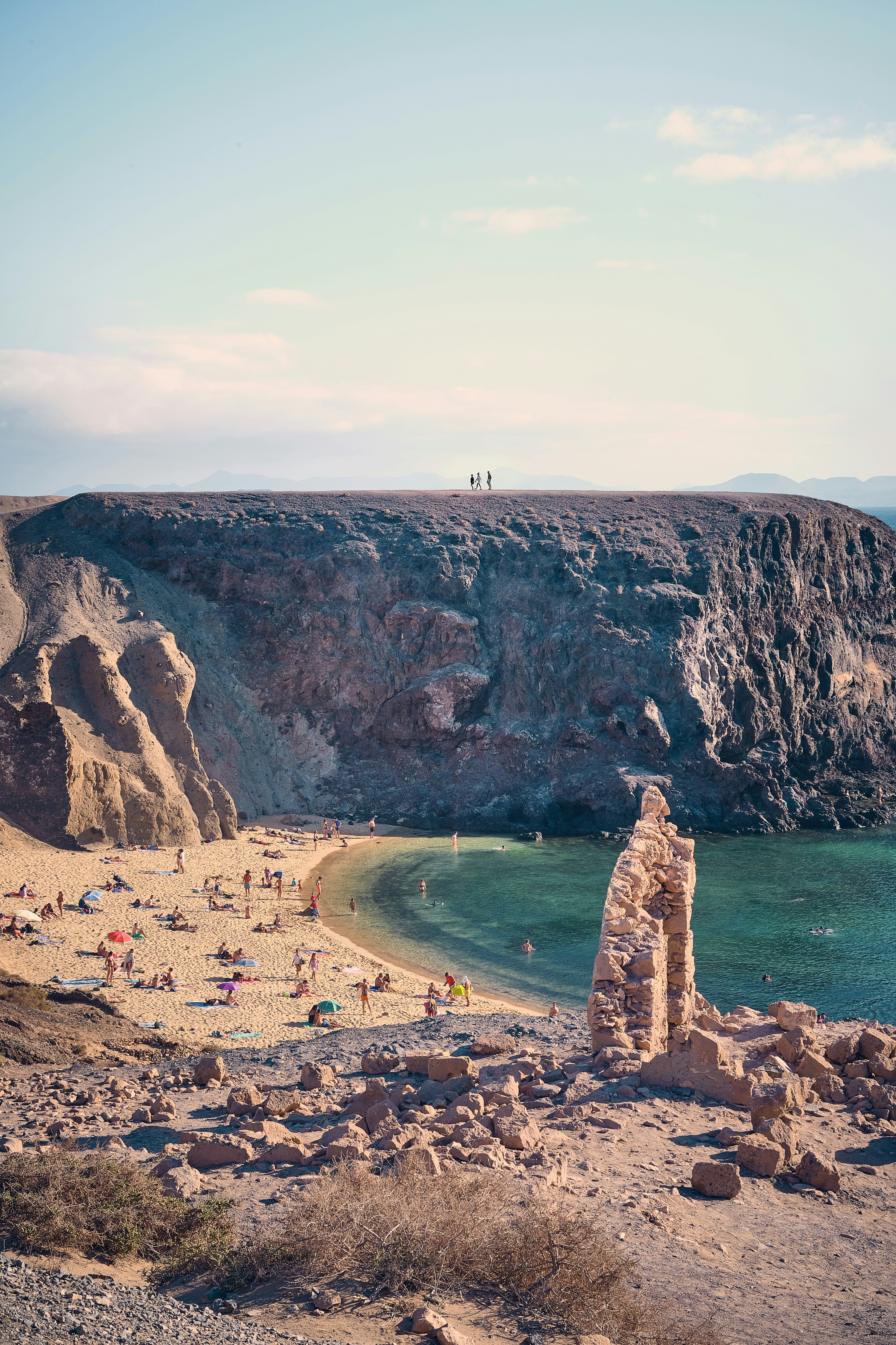 people on beach near brown rock formation during daytime