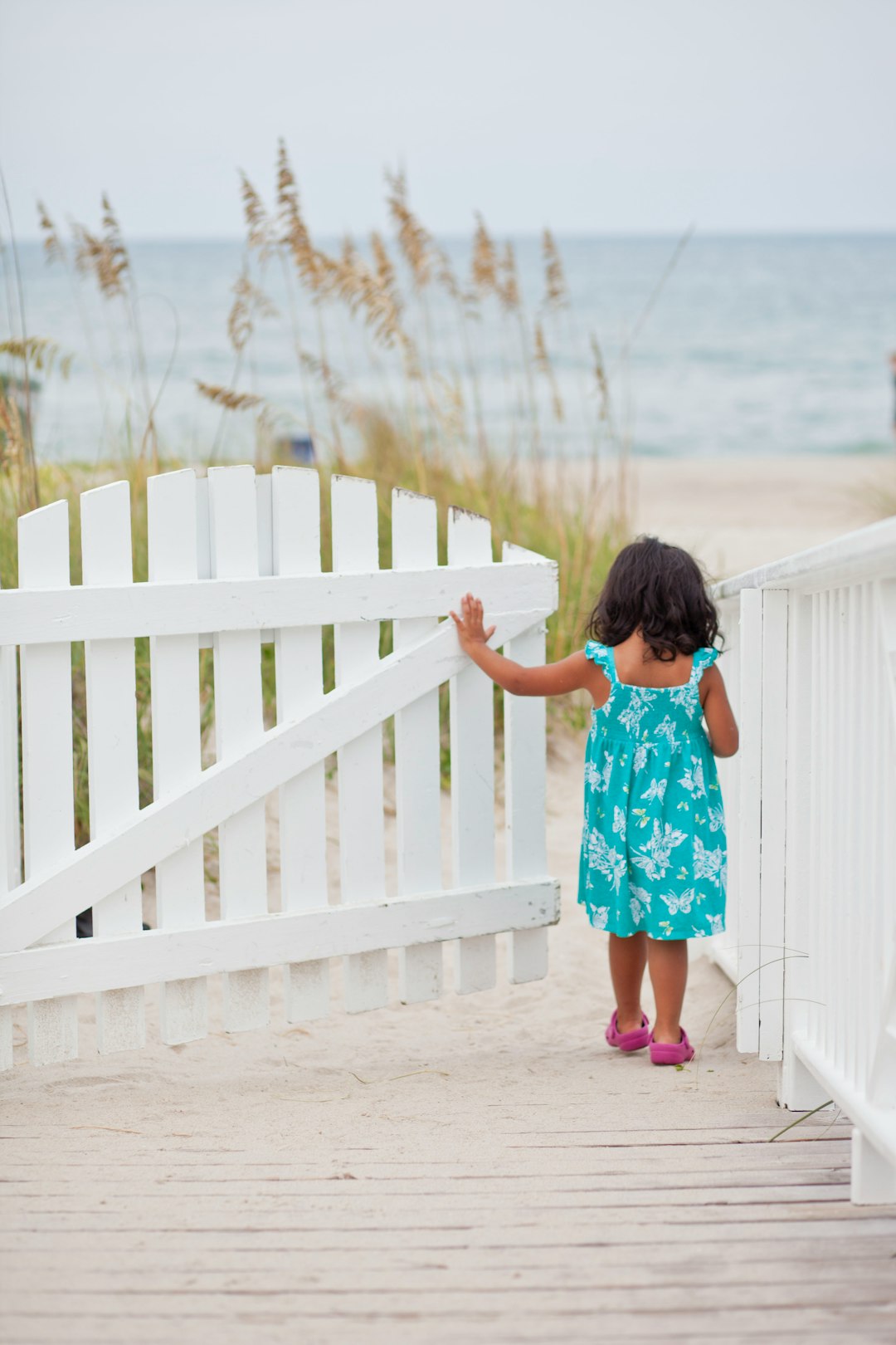 girl in white blue and red floral dress standing on white wooden fence during daytime