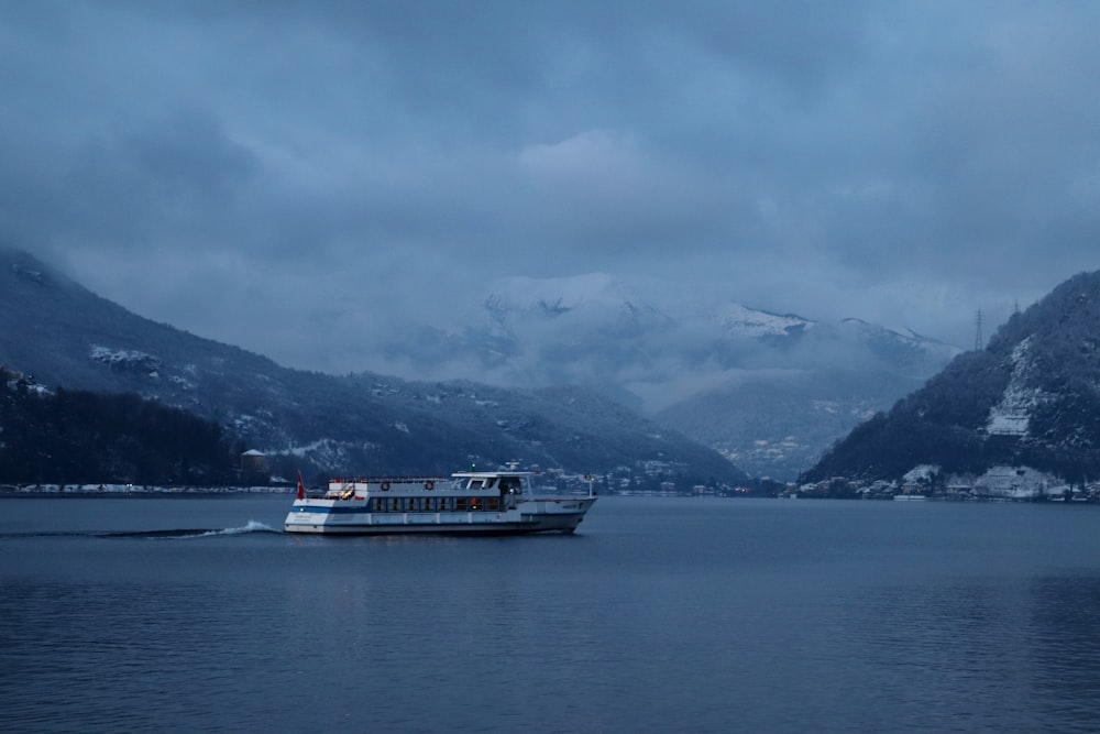 Navire blanc et noir sur la mer près des montagnes sous les nuages blancs pendant la journée