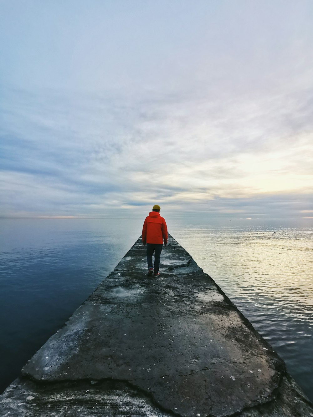 man in red hoodie standing on dock near body of water during daytime