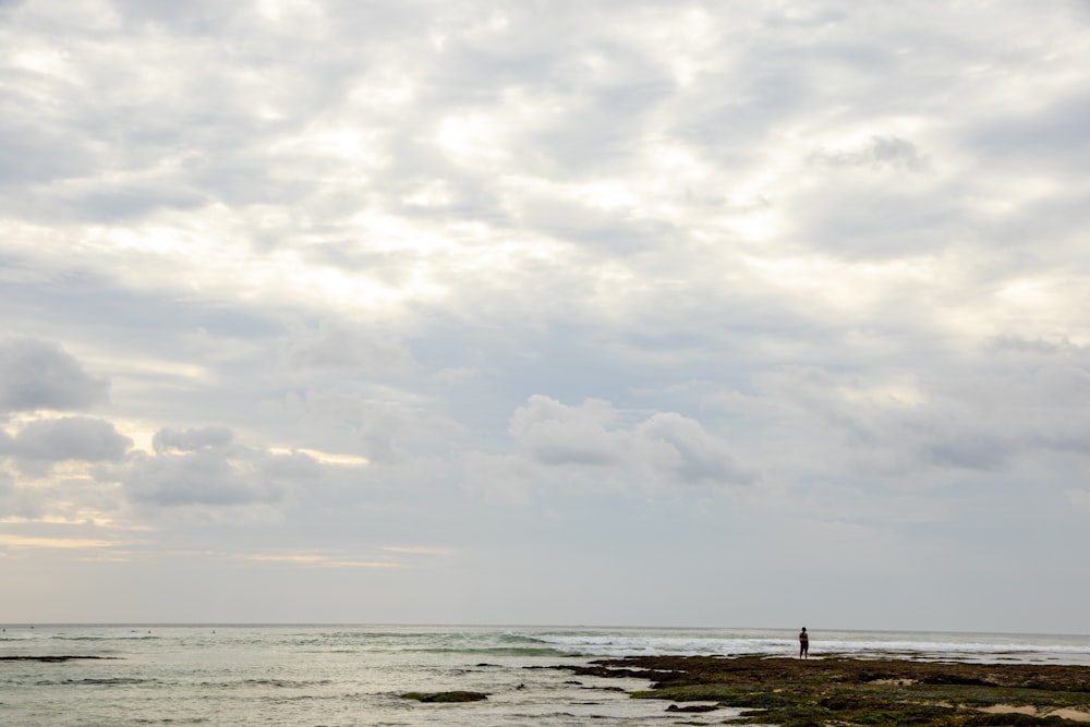 Person, die tagsüber unter bewölktem Himmel am Strandufer steht