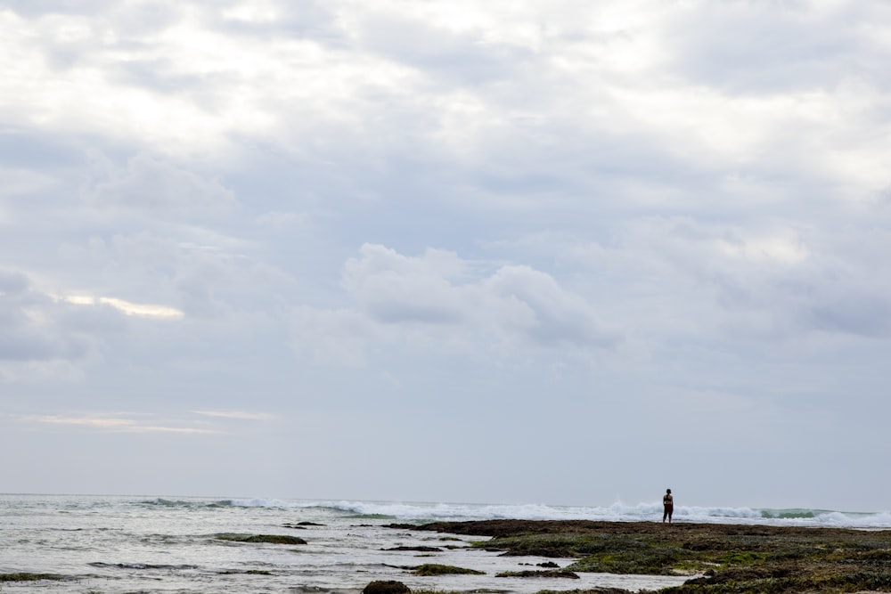 person standing on beach shore under cloudy sky during daytime