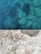 A concrete surface is shown in contrast with clear blue water. The concrete has visible small stones and pebbles embedded within, while beneath the water, large rocks are faintly visible, suggesting depth and transparency.