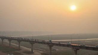 A wide shot of a large infrastructure bridge spanning a river with vehicles moving across under a clear sky.