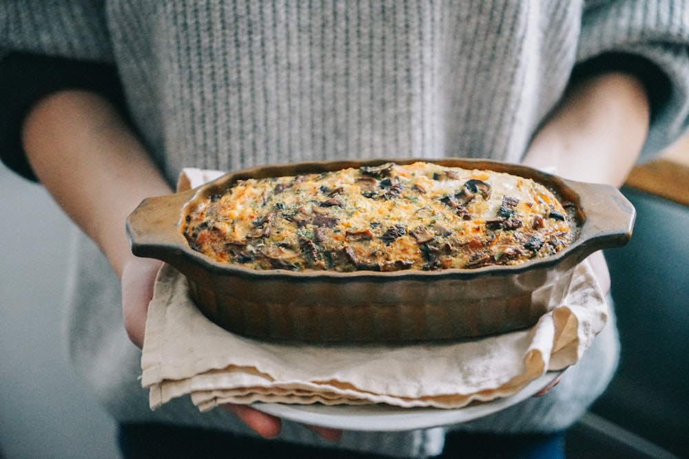 personne tenant une tarte brune et blanche sur une assiette en céramique blanche