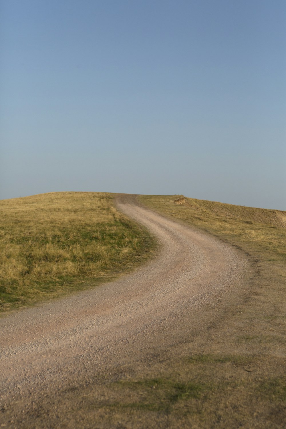 grauer Feldweg zwischen grünem Grasfeld unter blauem Himmel tagsüber