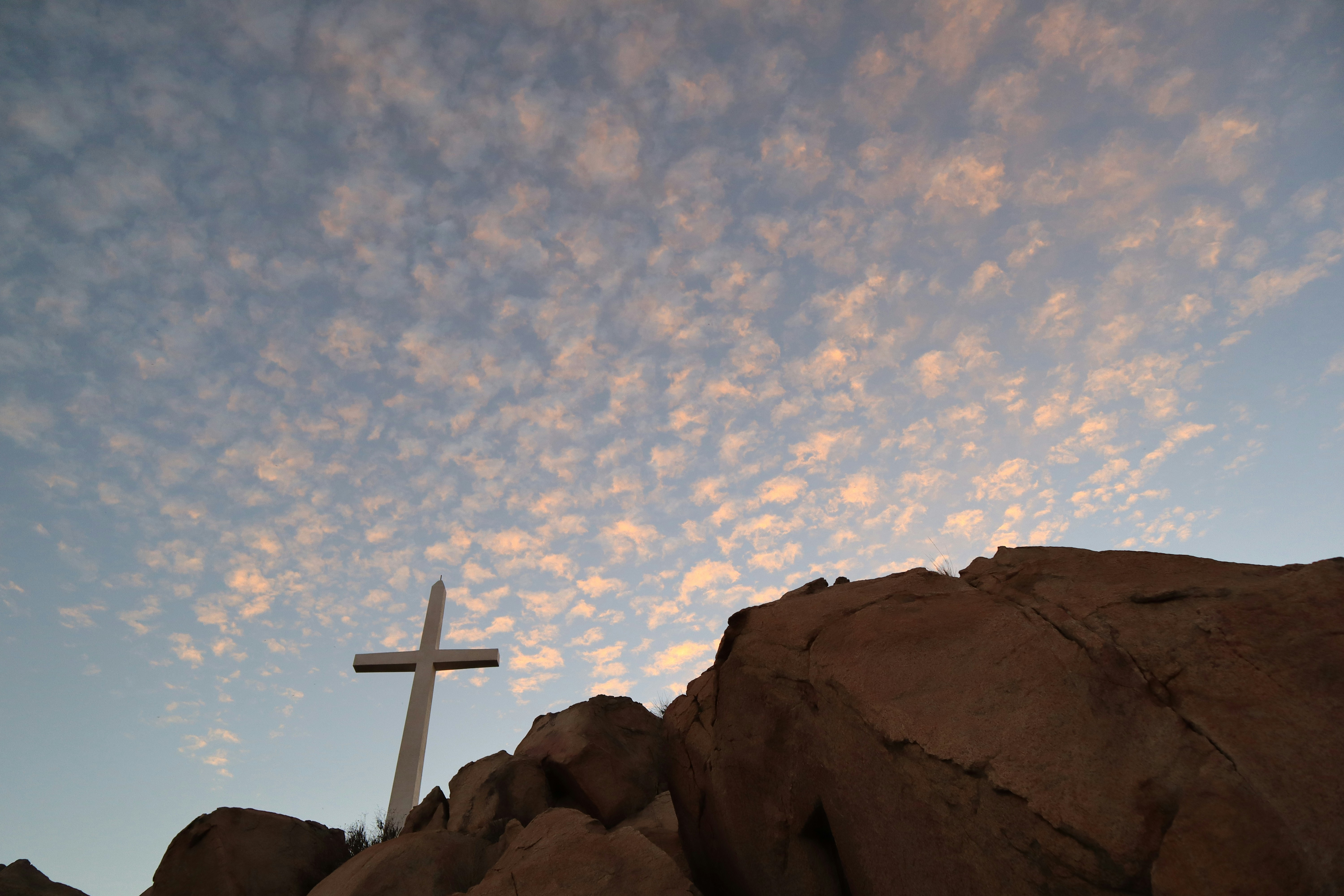 Illustrative photo: white cross on brown rock formation under blue sky during daytime