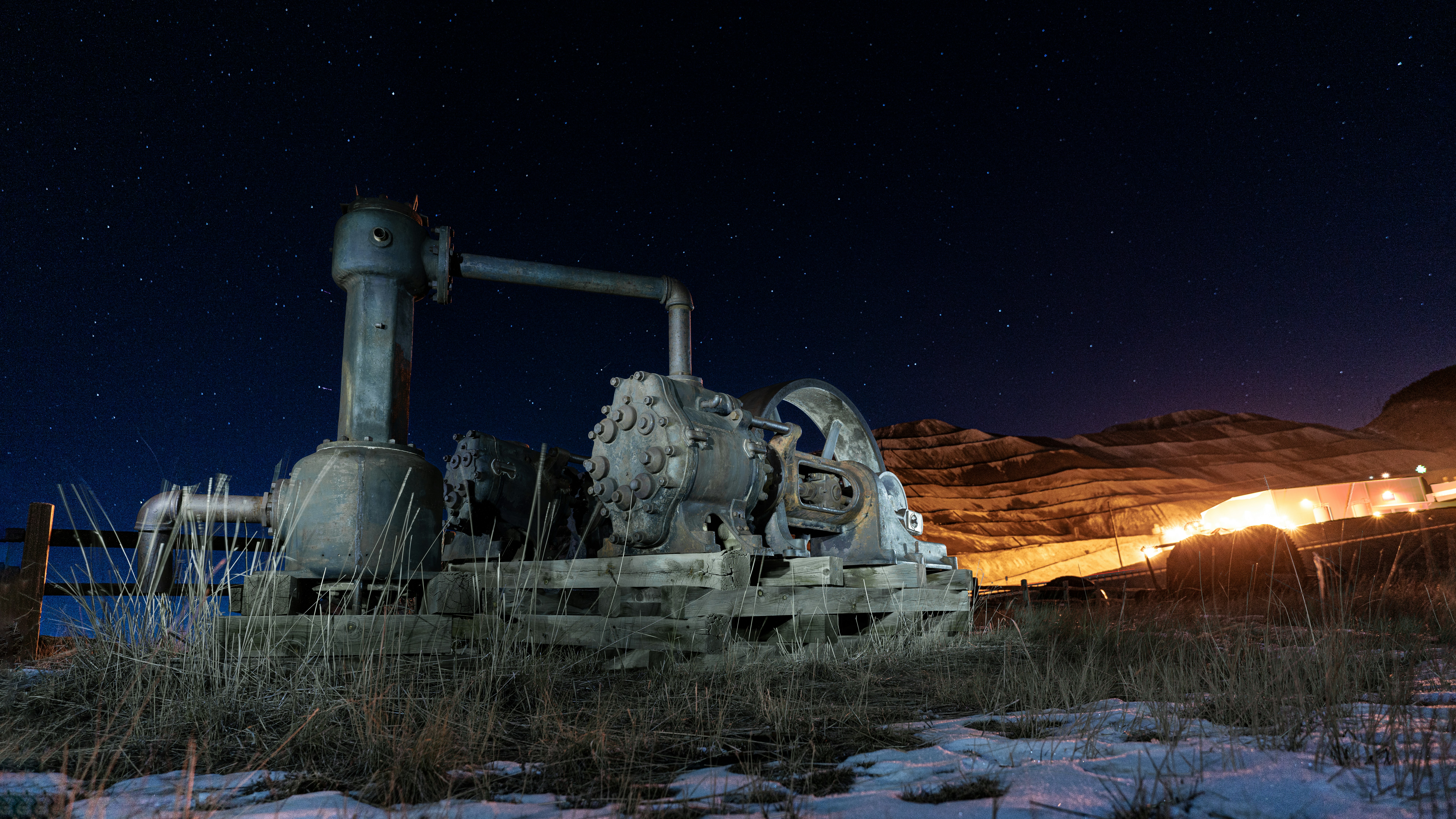 Gold mining machinery at night in a desert setting with base camp light bright in the background.