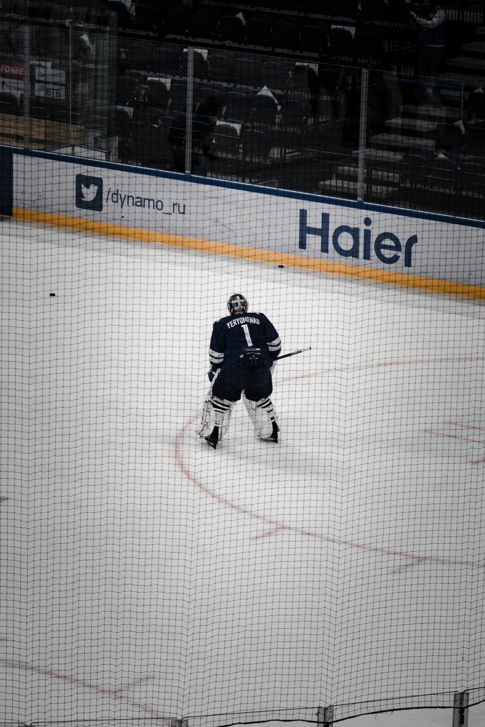 man in black and white ice hockey jersey shirt riding on black and white hockey stick