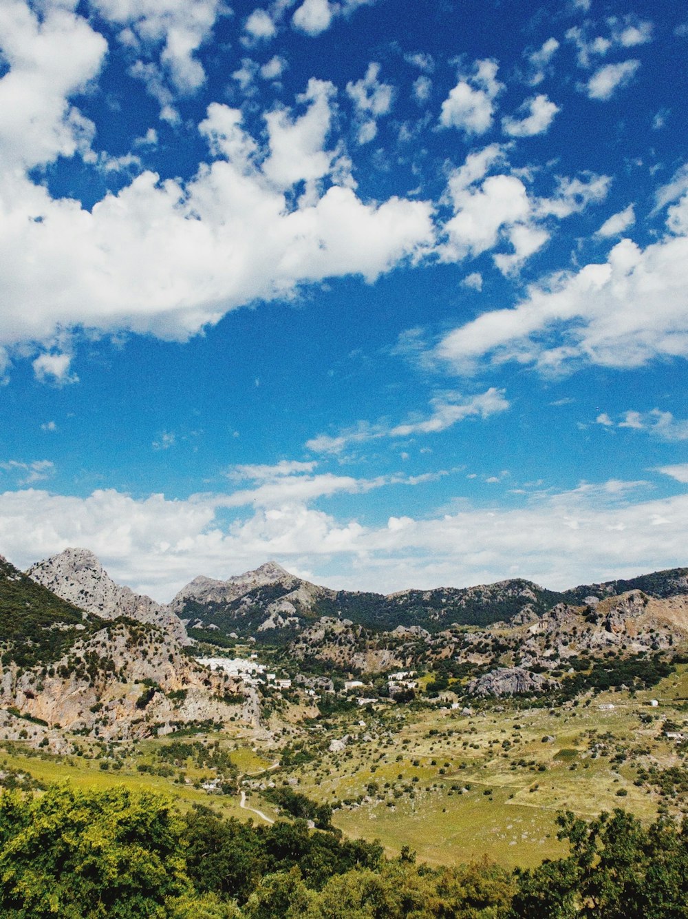 green grass field and mountains under blue sky and white clouds during daytime