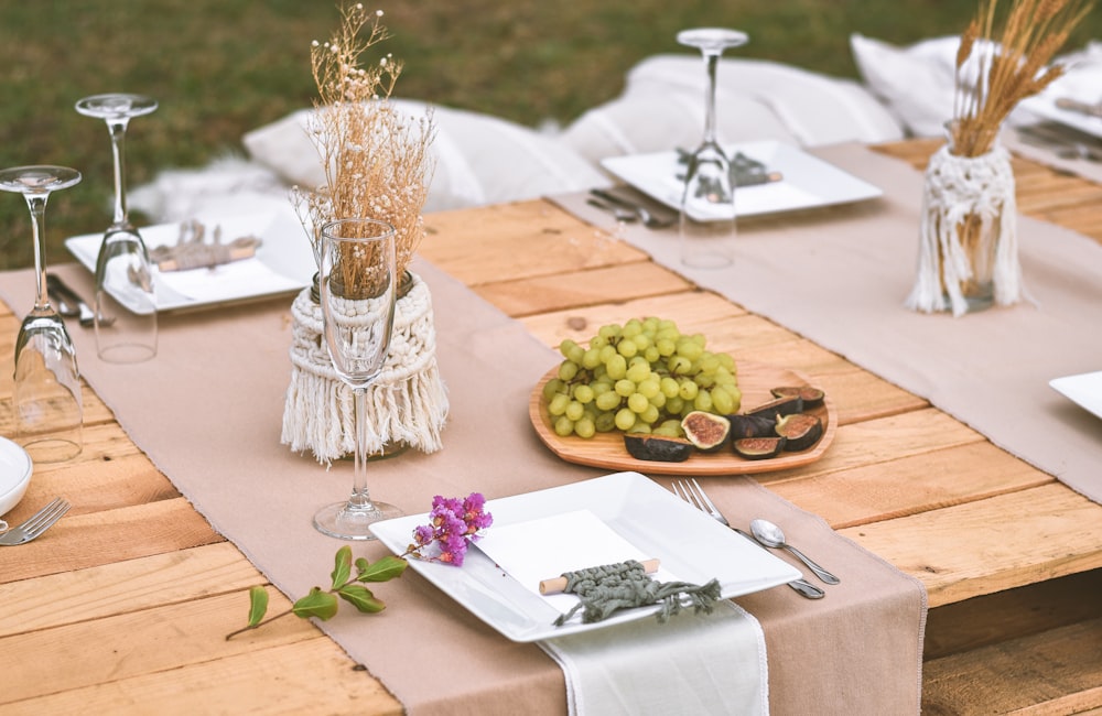 茶色の木製のテーブルの上にステンレス鋼のフォークとナイフの横の白いセラミックプレートに緑のブドウ