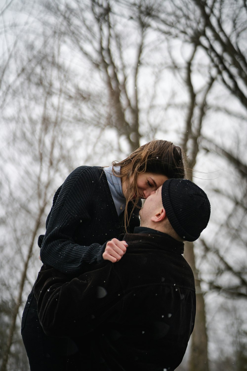 woman in black coat and black knit cap standing near bare trees during daytime