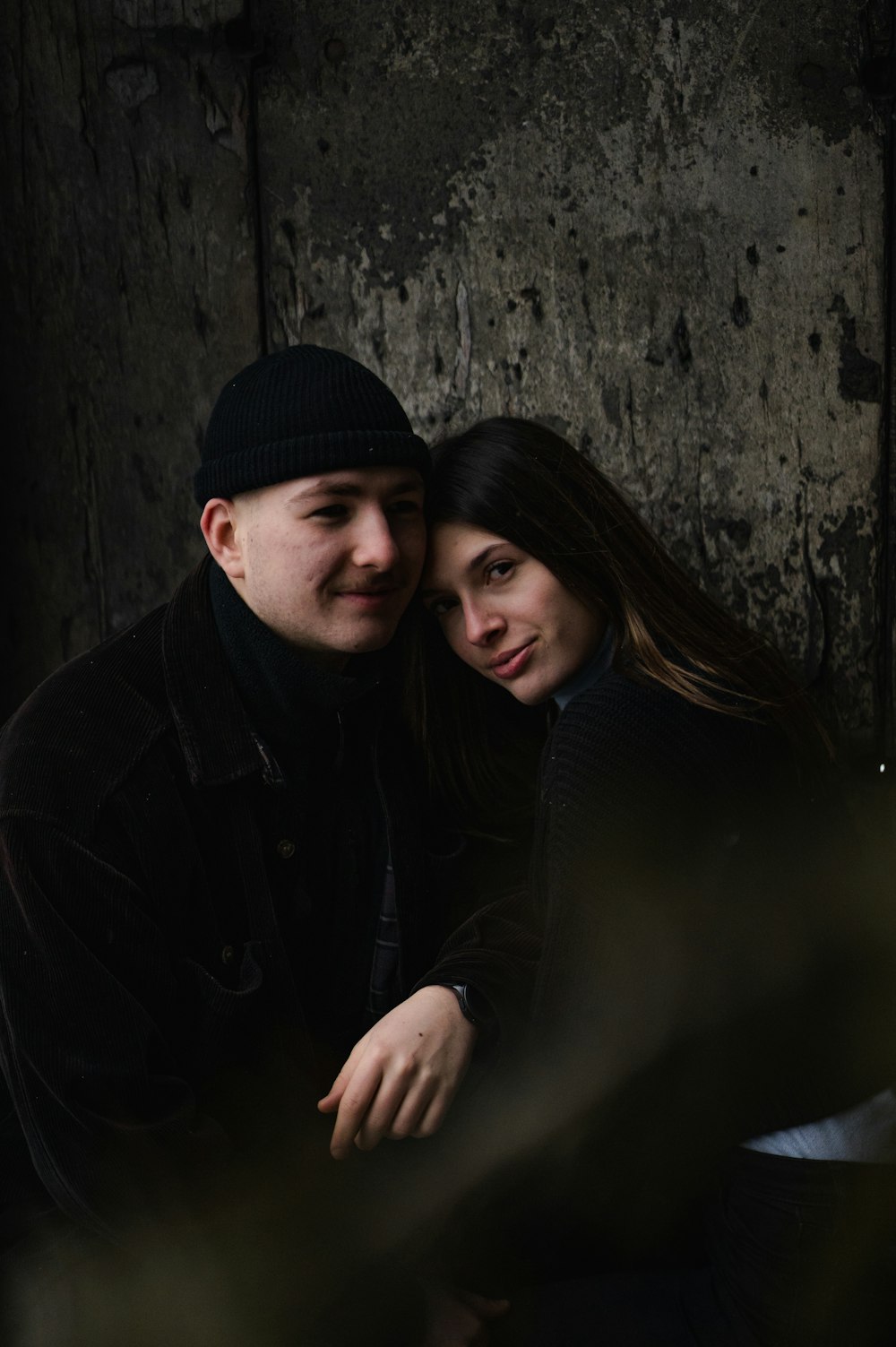 man in black knit cap and black jacket hugging woman in black knit cap