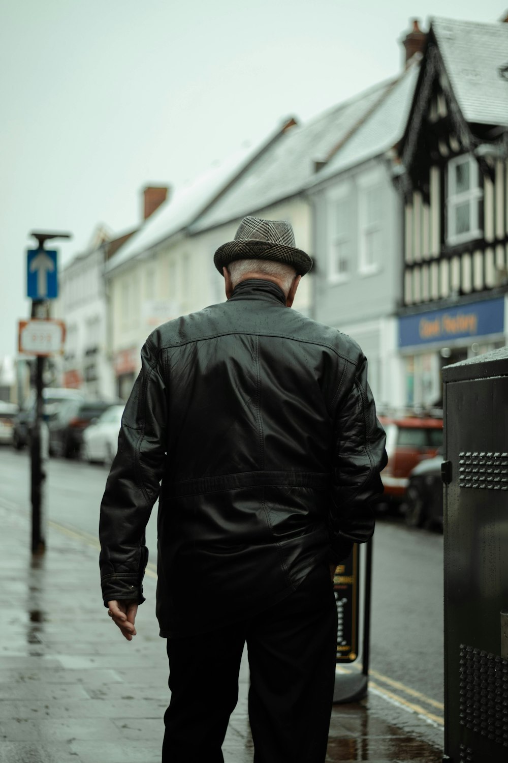 man in black leather jacket standing on sidewalk during daytime