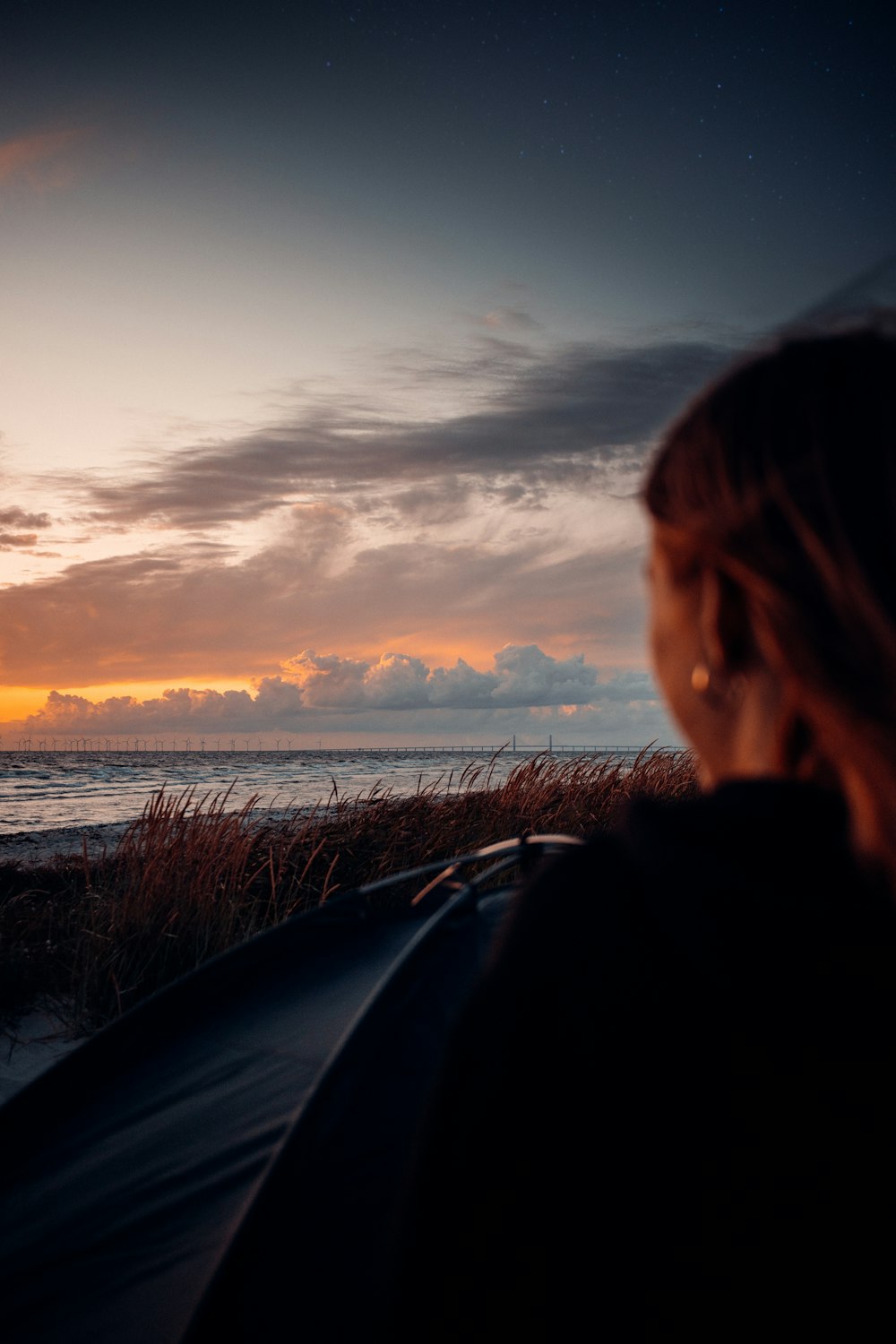 woman in black jacket standing near body of water during sunset